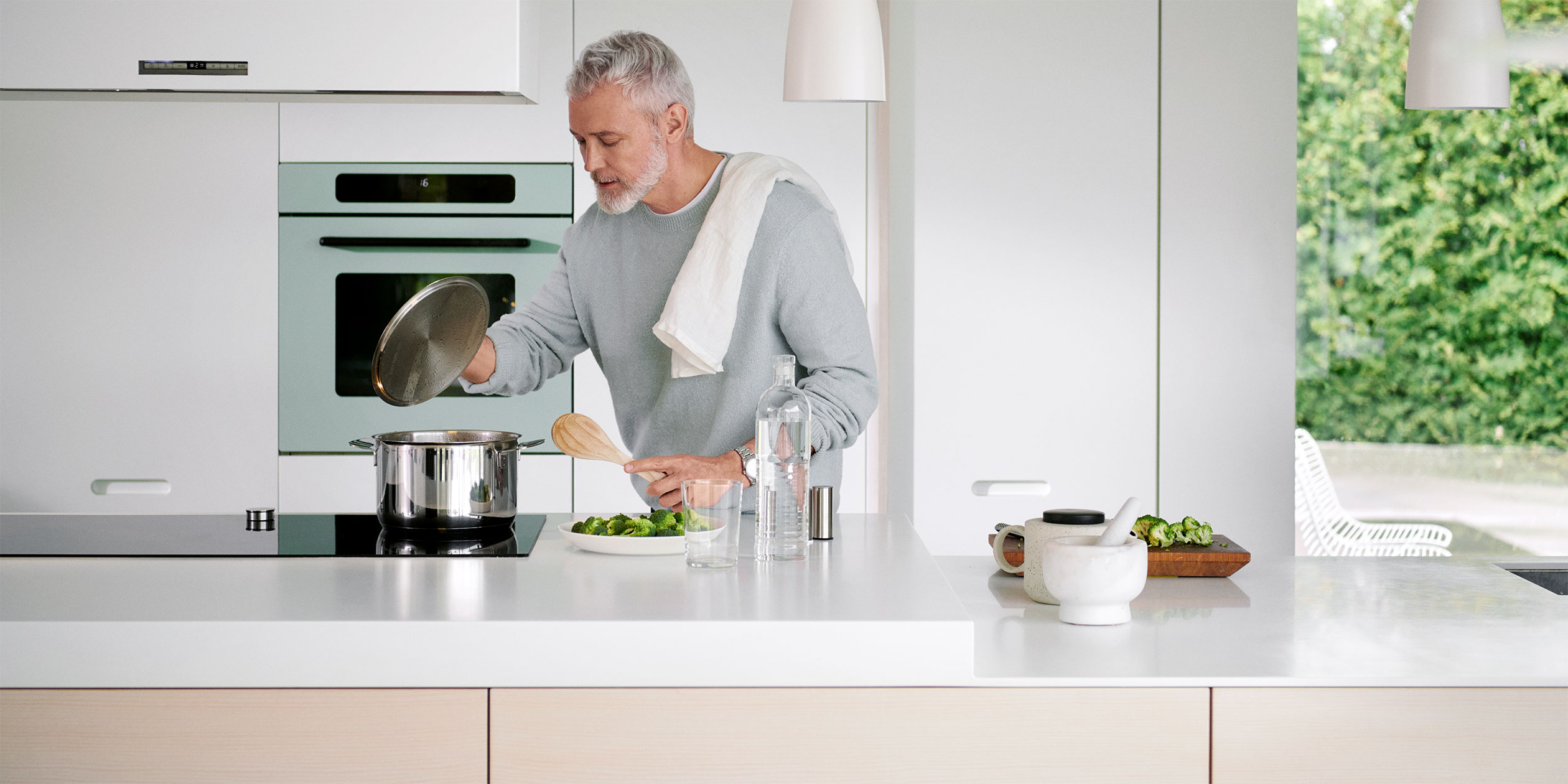 En äldre man lagar mat i ett vitt kök.