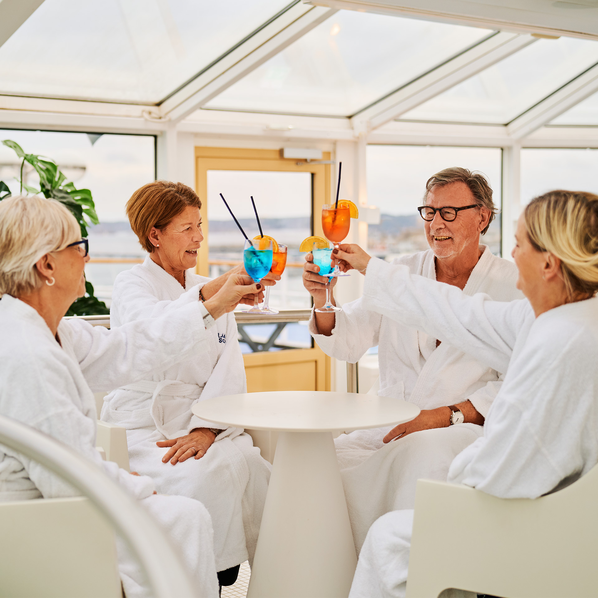 Fyra äldre män och kvinnor skålar på spa iklädda vita morgonrockar.