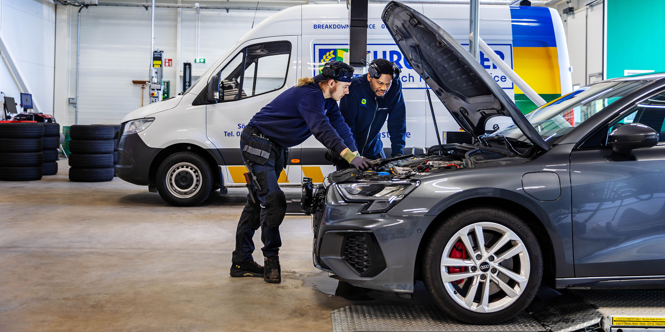 Två män tittar under motorhuven på en bil på en Euromaster verkstad.
