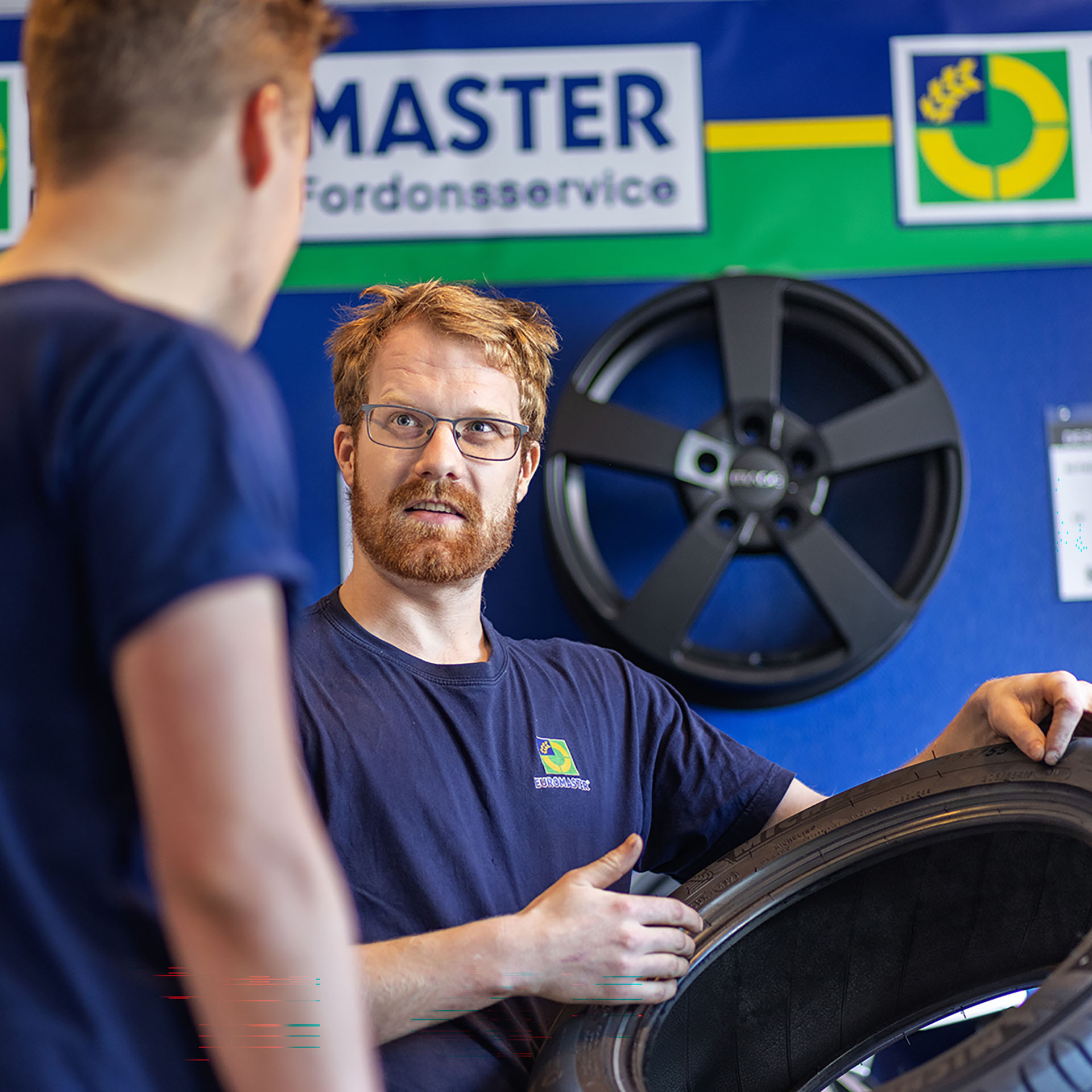 En bilservicetekniker på Euromaster demonstrerar ett däck för en annan person.