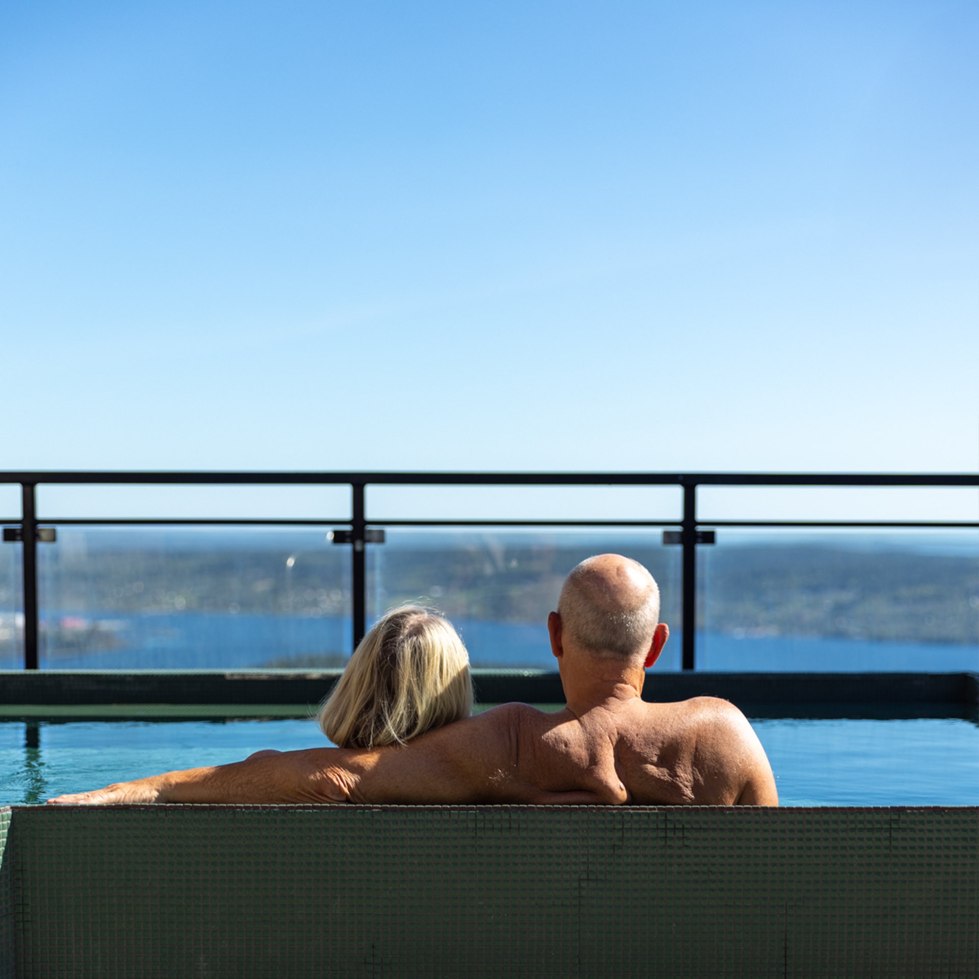 Baksidan på ett äldre par som sitter i en pool och tittar på utsikten nedanför.