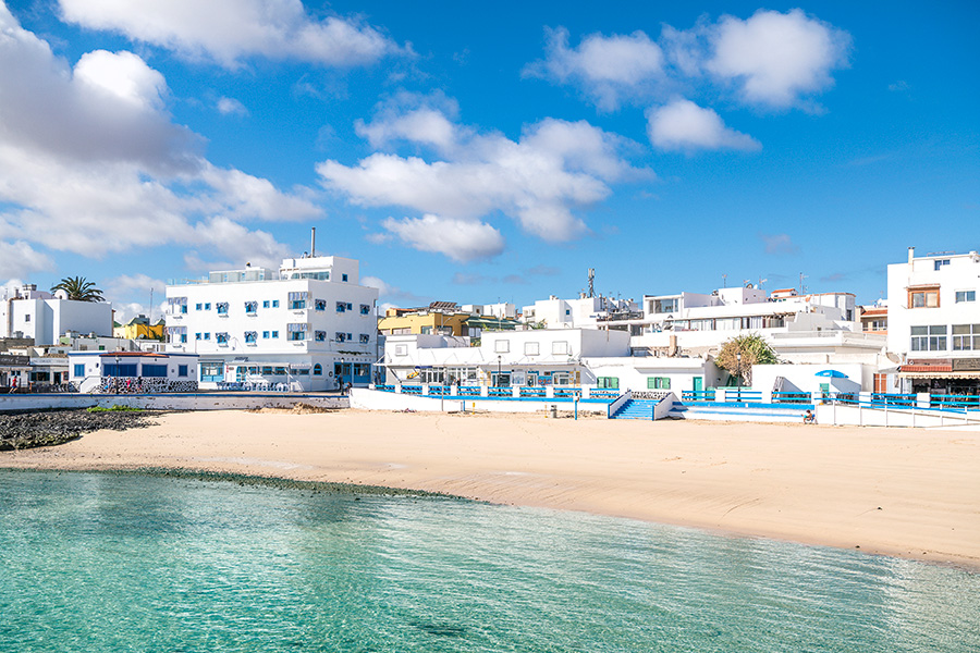 Ett vitt hotell vid en strandremsa med turkost vatten.